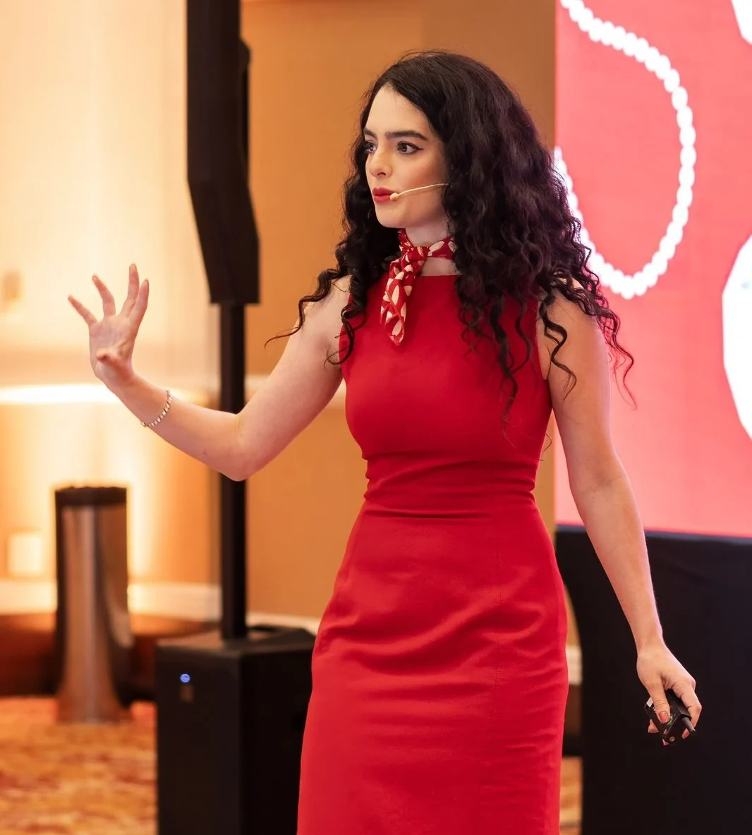 Diandra Santos no palco, de vestido vermelho, durante uma palestra